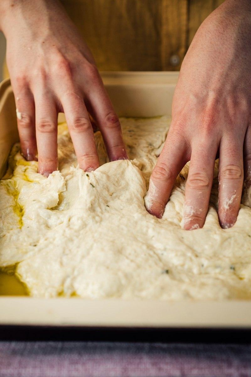 Mani che stendono l'impasto della focaccia nella teglia