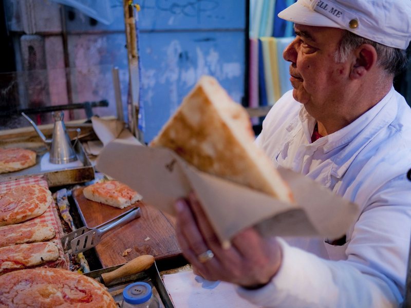 Un pizzaiolo passa un trancio di pizza al taglio sul banco